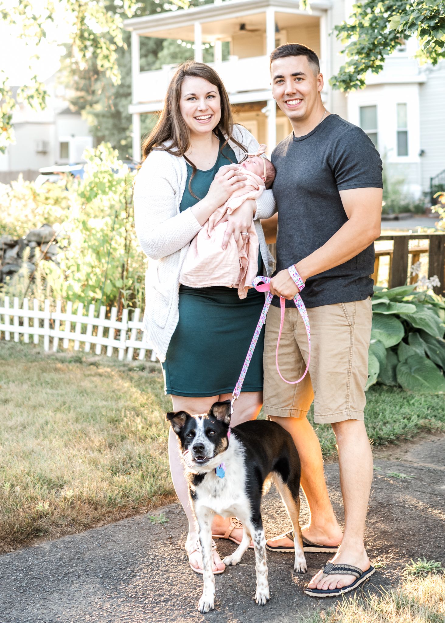 Family with dog standing outside their home on sunny day.