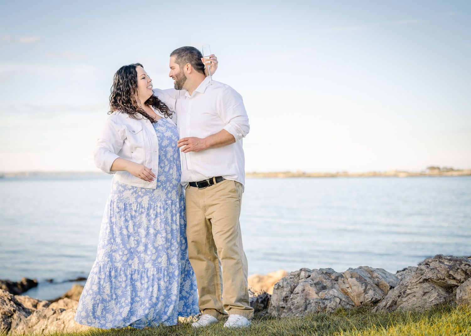 A couple in coordinated white and blue outfits poses together on rocky coastal terrain.