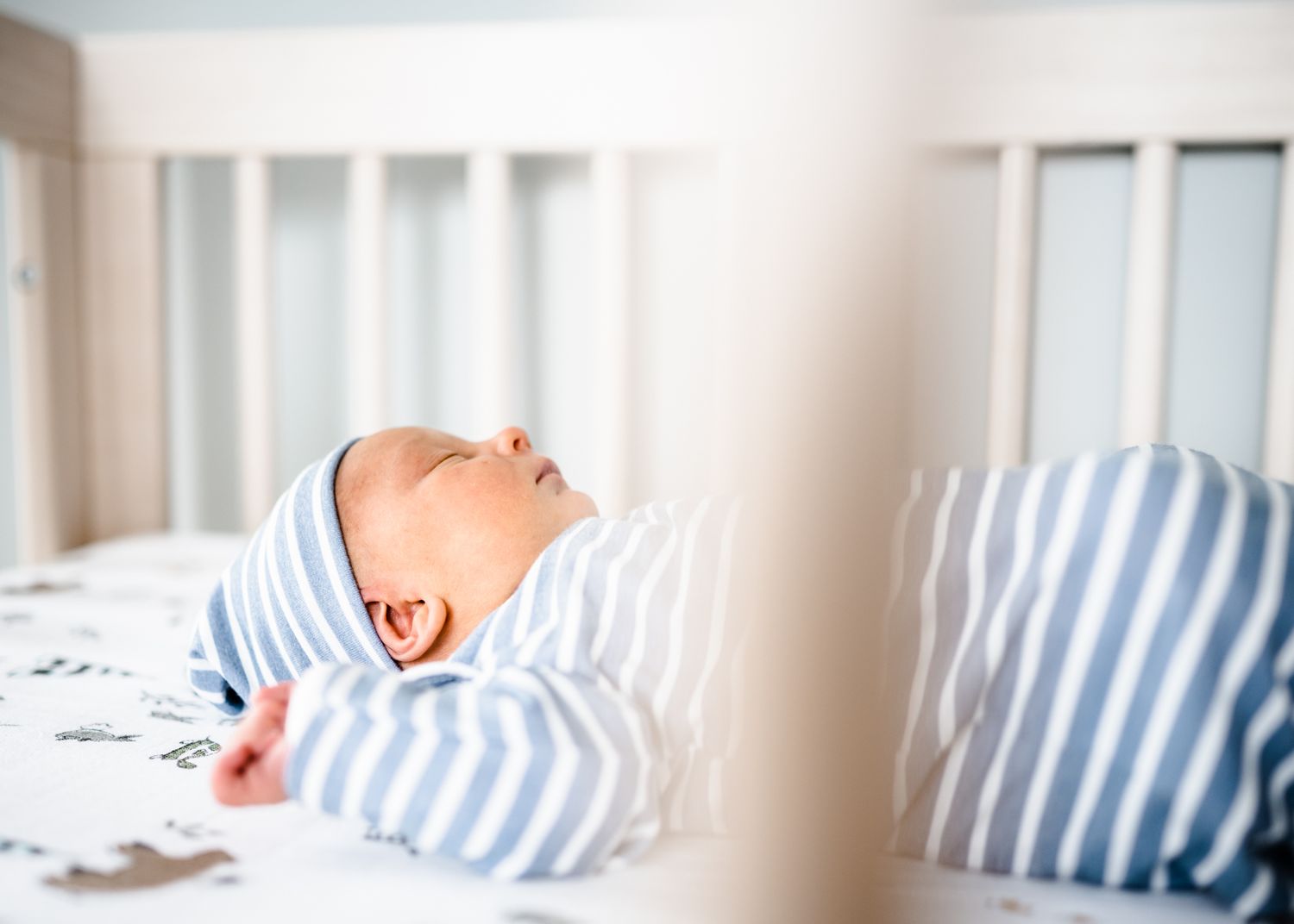 Peaceful baby wearing striped outfit sleeping in white crib.