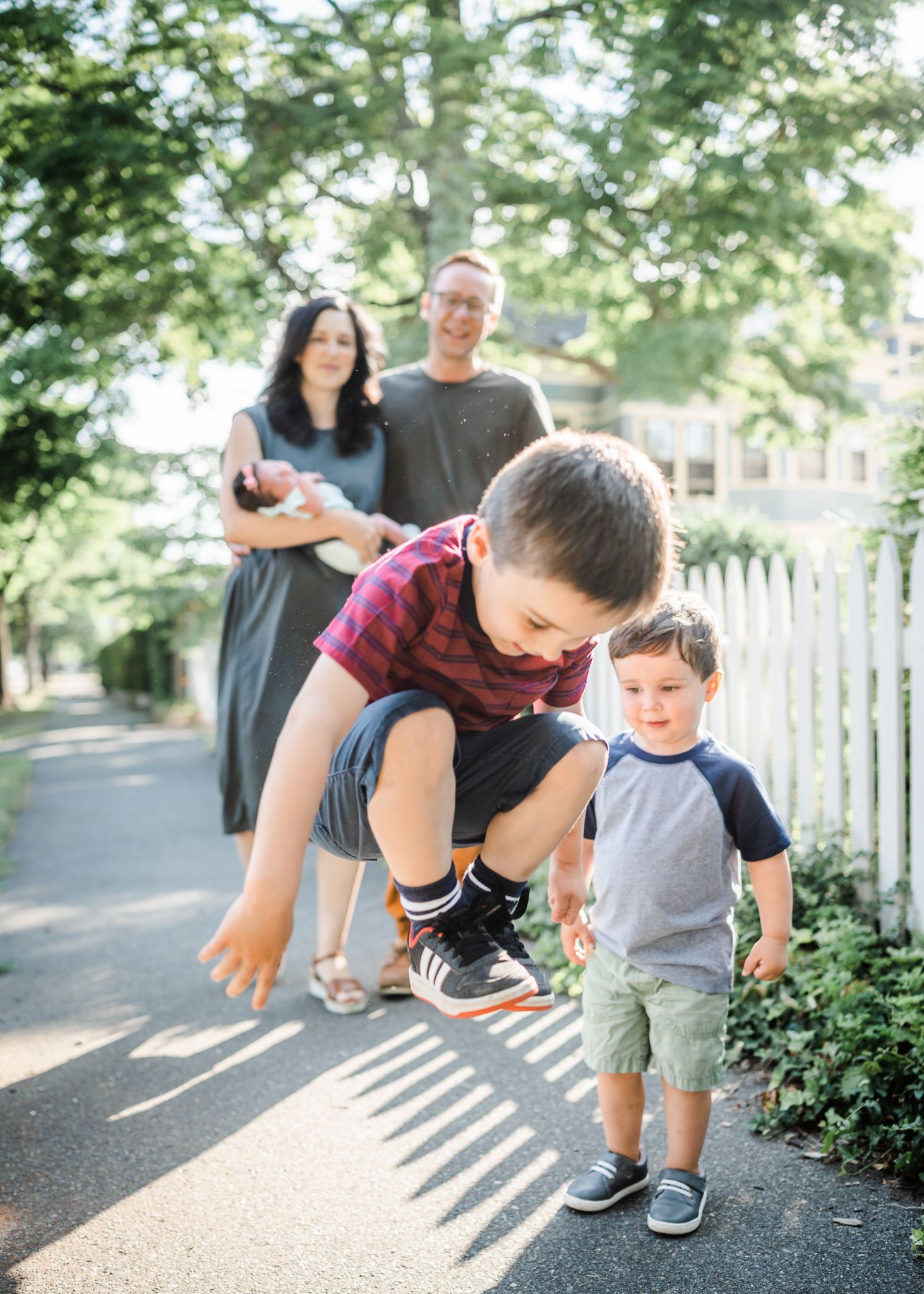 Family enjoying a playful moment together outdoors on a sunny path with shadows cast across the ground.