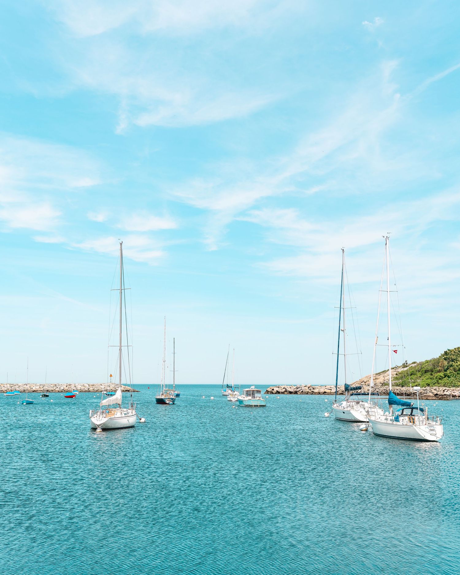 Multiple sailboats and yachts anchored in calm turquoise waters under bright blue skies on a sunny day.