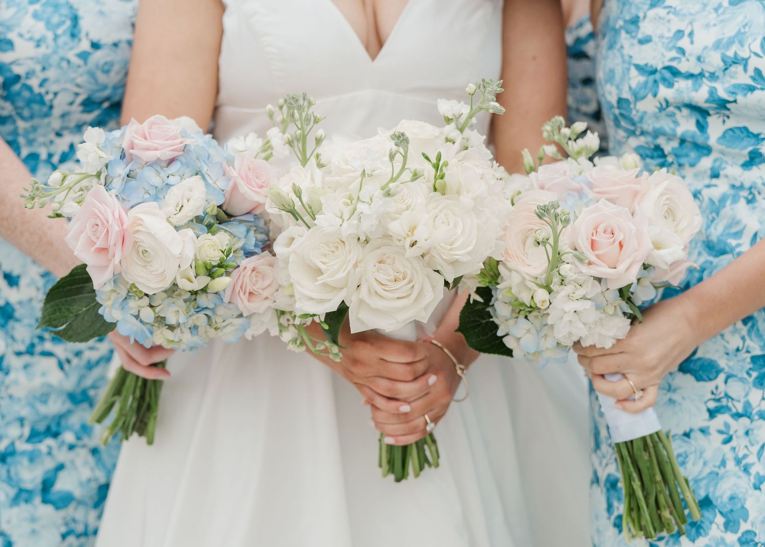Close-up of bridesmaids holding romantic pink and white wedding bouquets with roses and baby's breath against blue fabric.