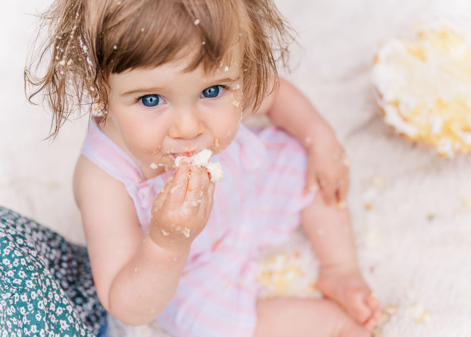 Child in pink dress eating cake during celebration with messy hands.