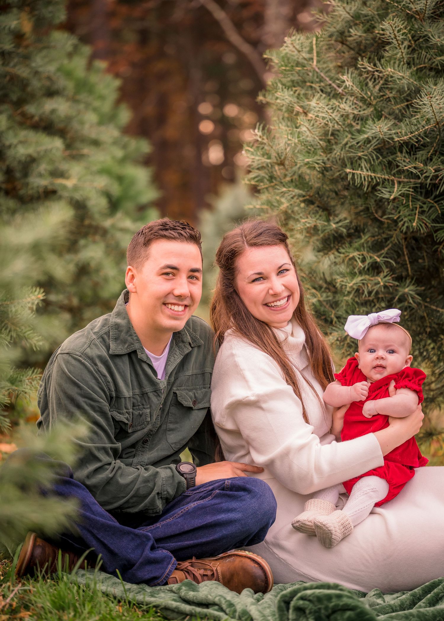 Family sitting together on blanket surrounded by evergreen trees during outdoor photo session.