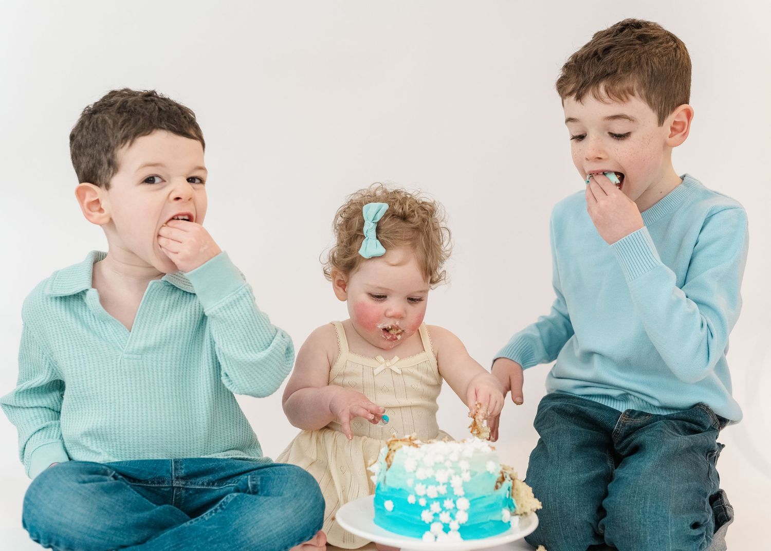 Cake smash. Baby and big siblings eating a blue cake together with a white background.
