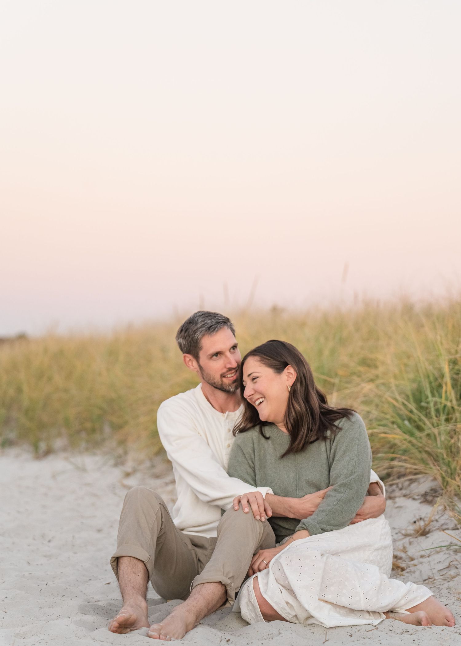 A couple relaxes together on a sandy beach during sunset while sharing intimate laughter.