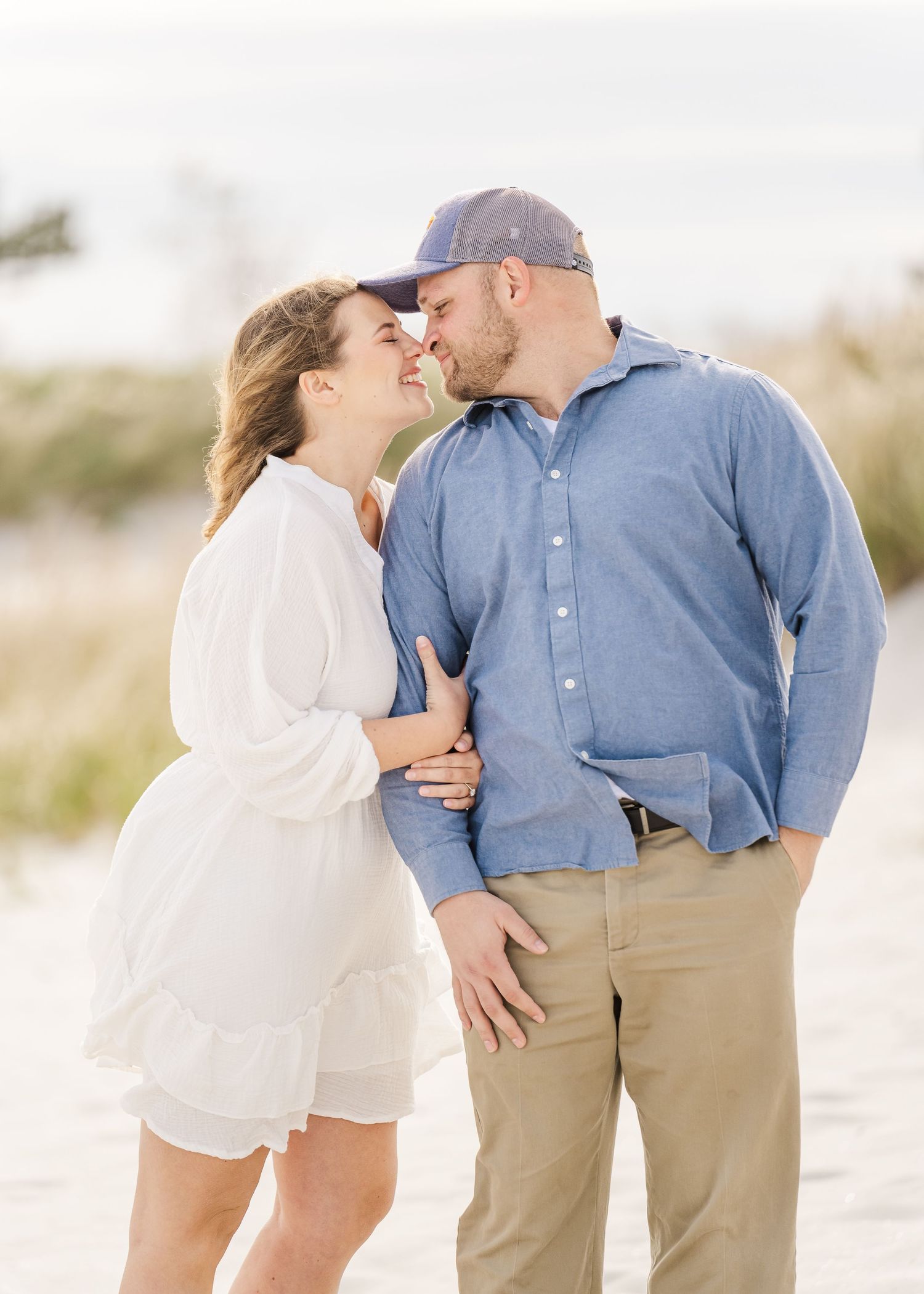 A romantic moment captured between a couple on a beach with sand dunes in the background.
