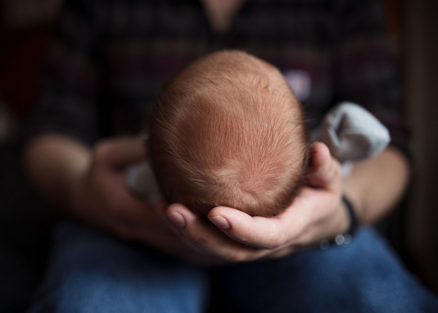 Gentle hands cradle a tiny newborn's head against a dark background.