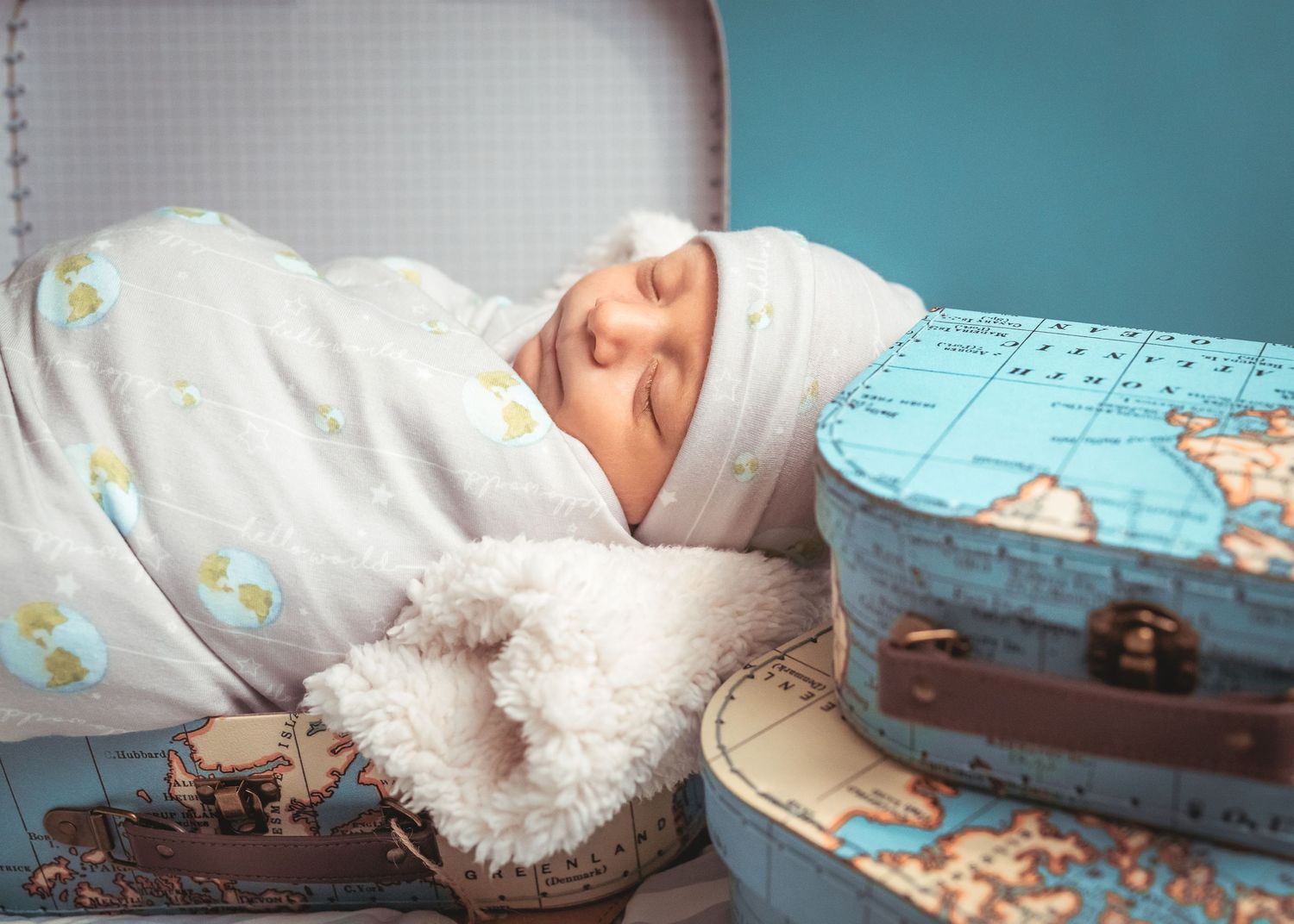 A sleeping baby wrapped in white with vintage suitcases in soft blue tones.