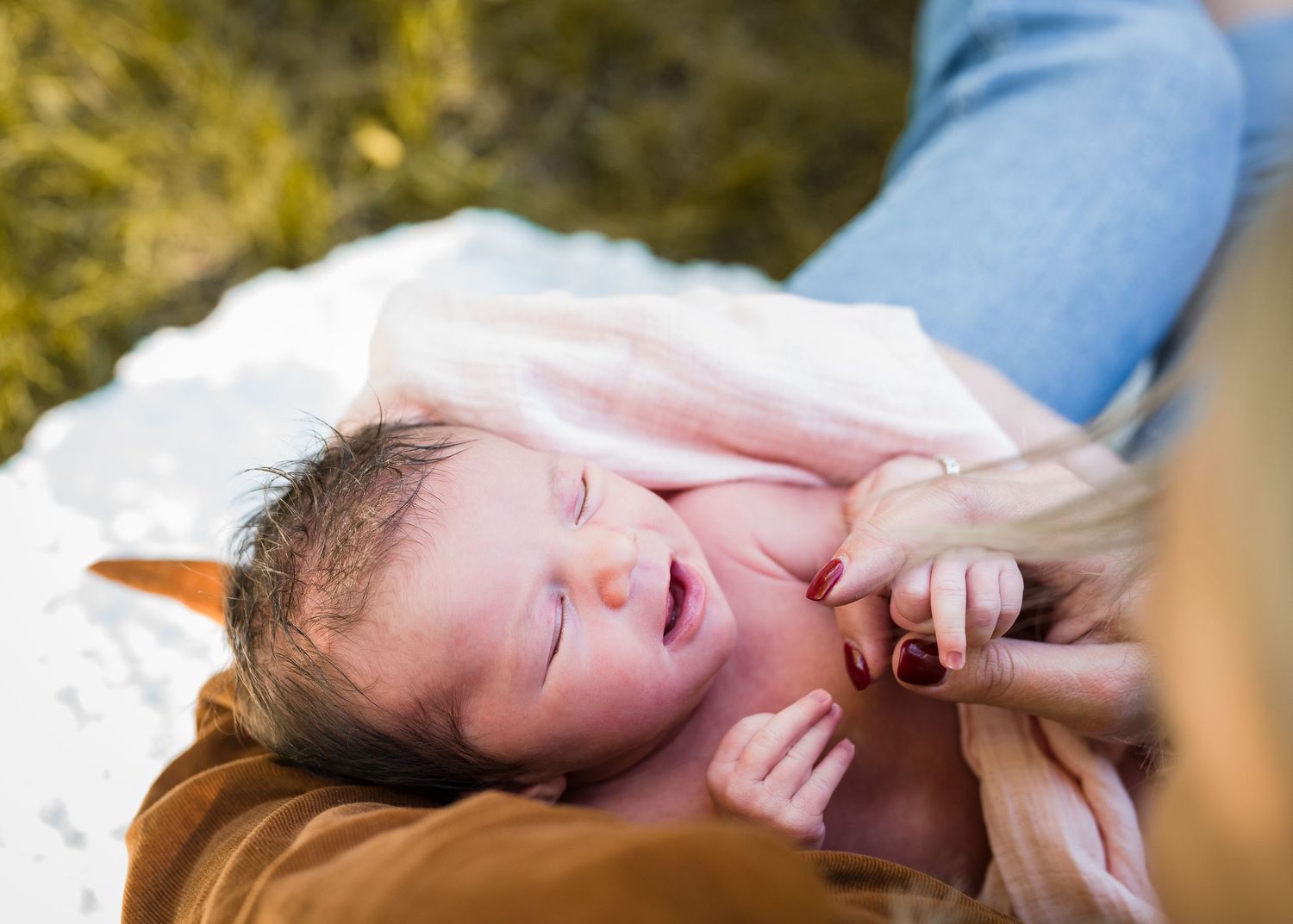 Newborn baby yawning while resting on brown clothing.