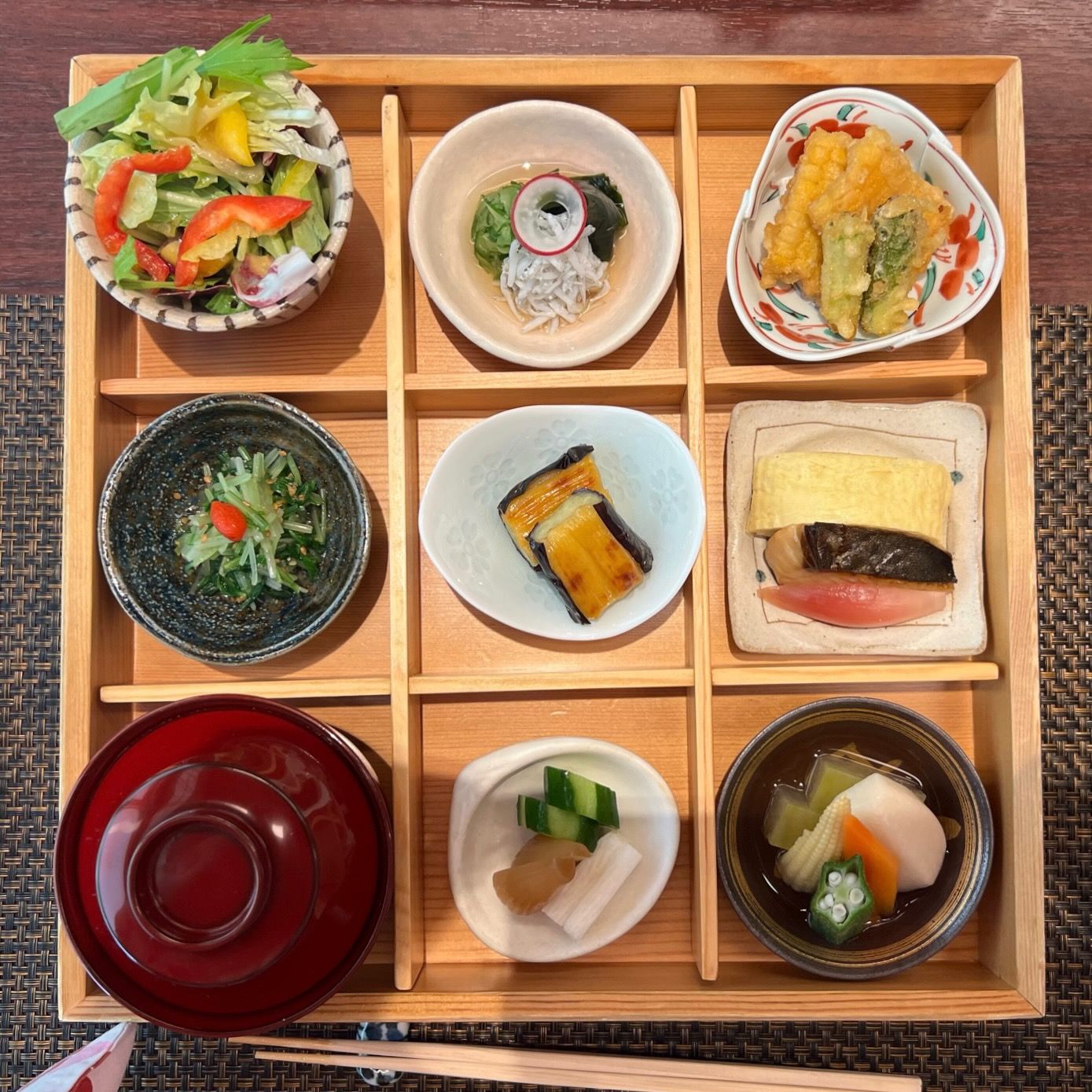 Traditional Japanese bento box featuring nine compartments with various colorful dishes and sides.