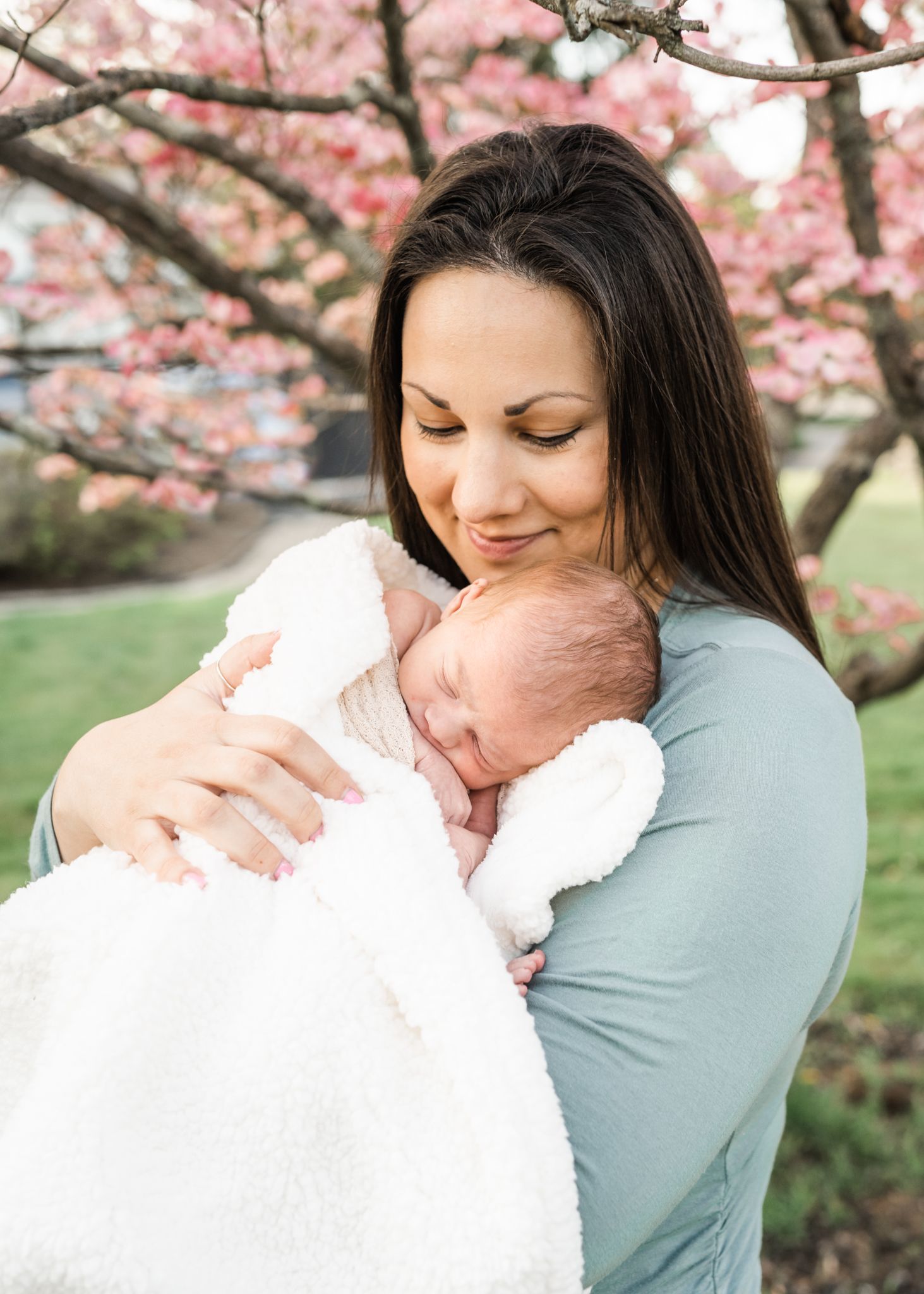 A tender moment between parent and newborn under flowering cherry blossom trees.