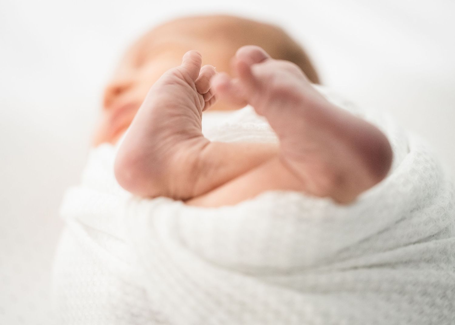 Close up of newborn baby feet wrapped in soft white blanket.