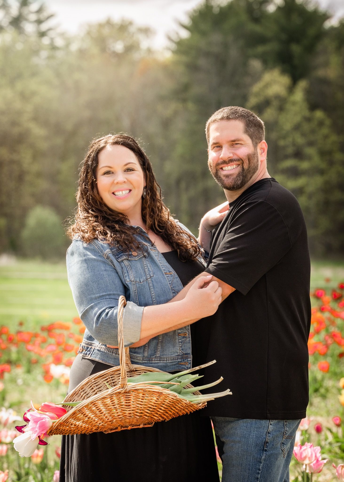 Couple poses with wicker basket in spring tulip garden.