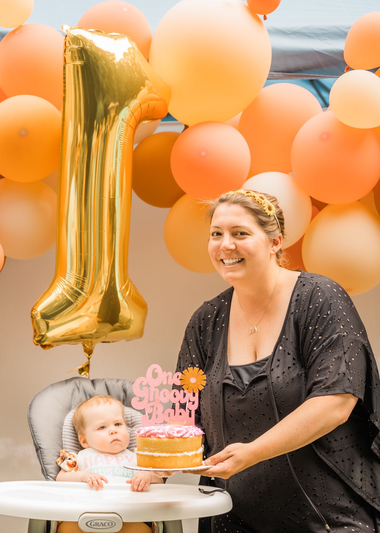 First birthday celebration with peach balloons, gold number one balloon, and pink birthday cake.