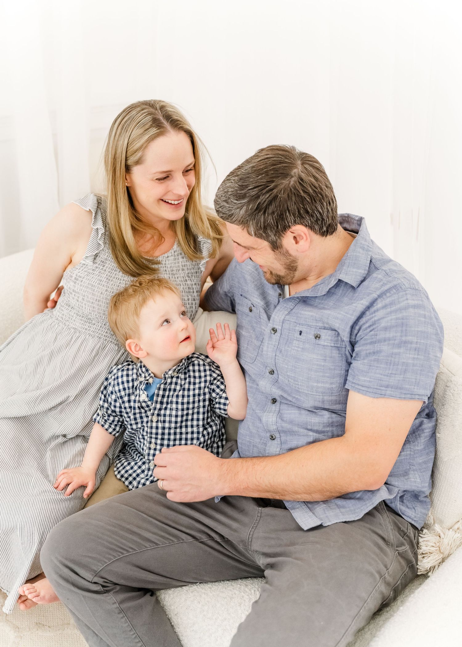 A family shares a tender moment together while relaxing on white bedding and wearing coordinated blue and grey outfits.