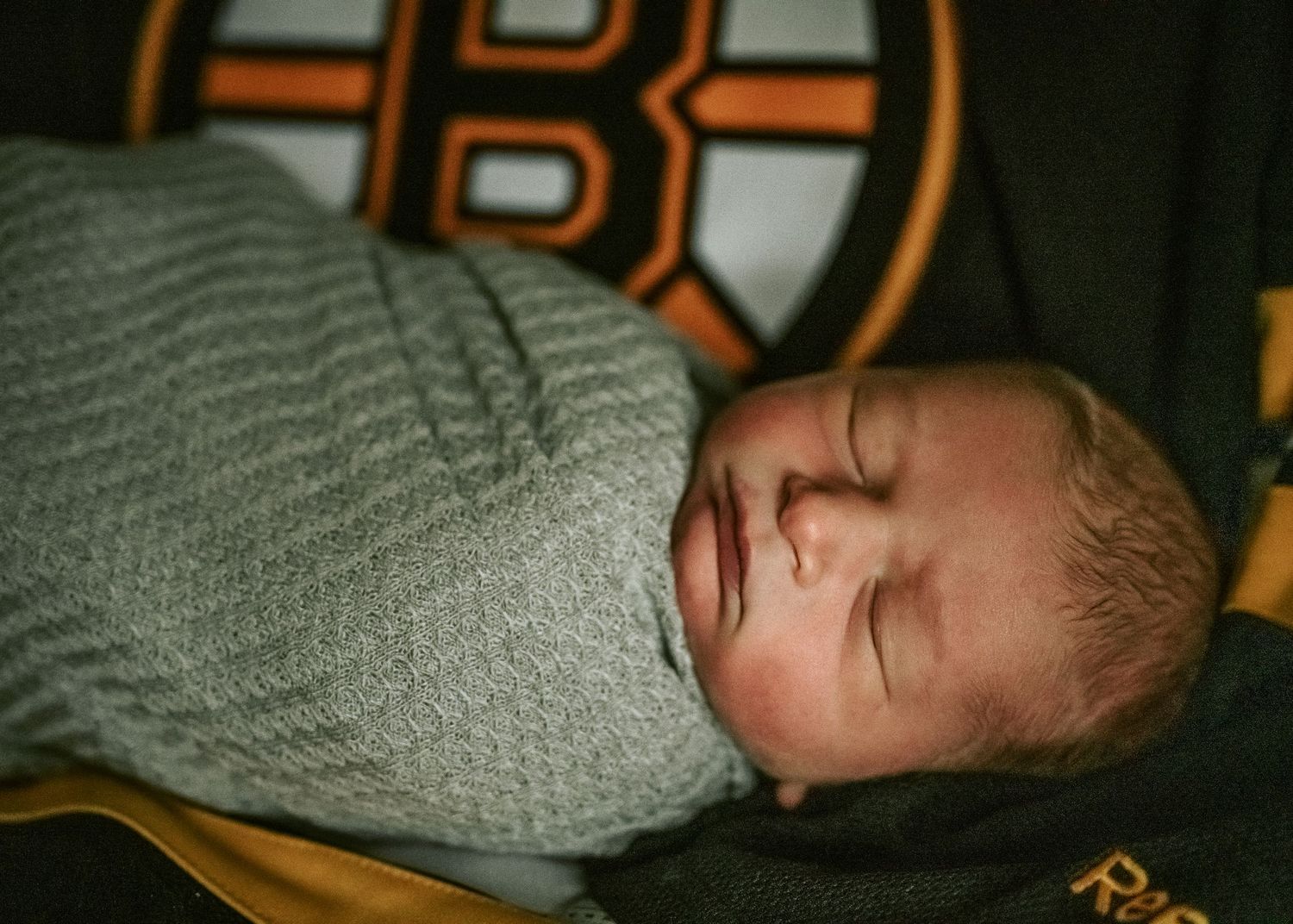 Sleeping baby wearing grey clothing against a Boston Bruins background.