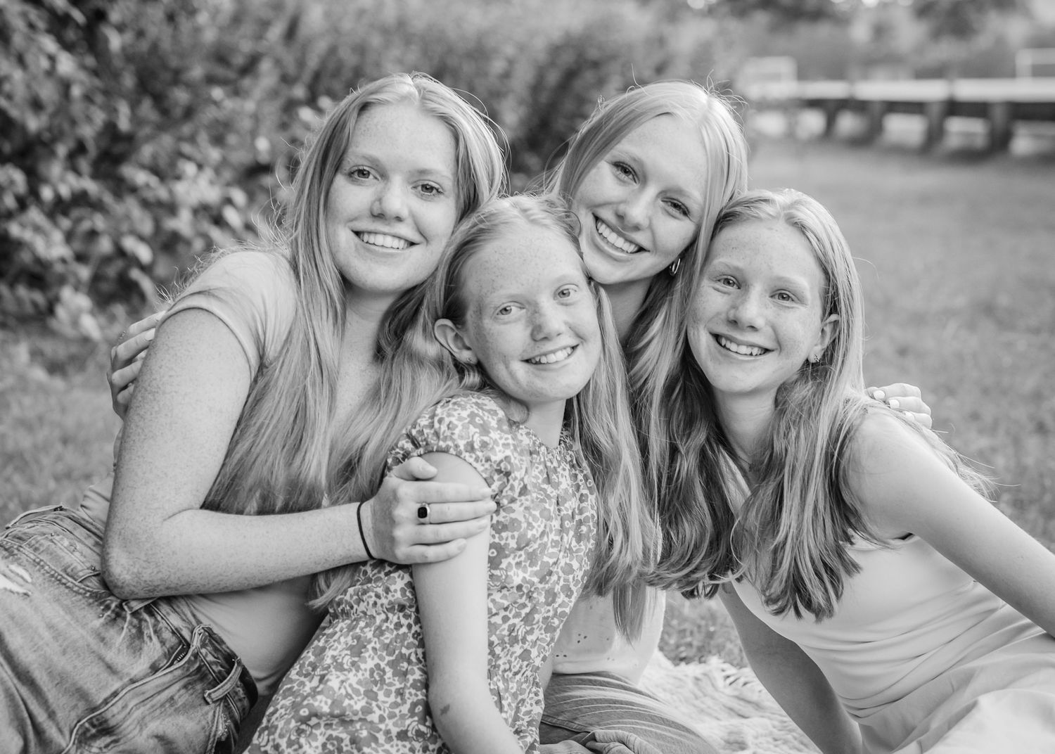 Black and white portrait of four sisters embracing and smiling outdoors.