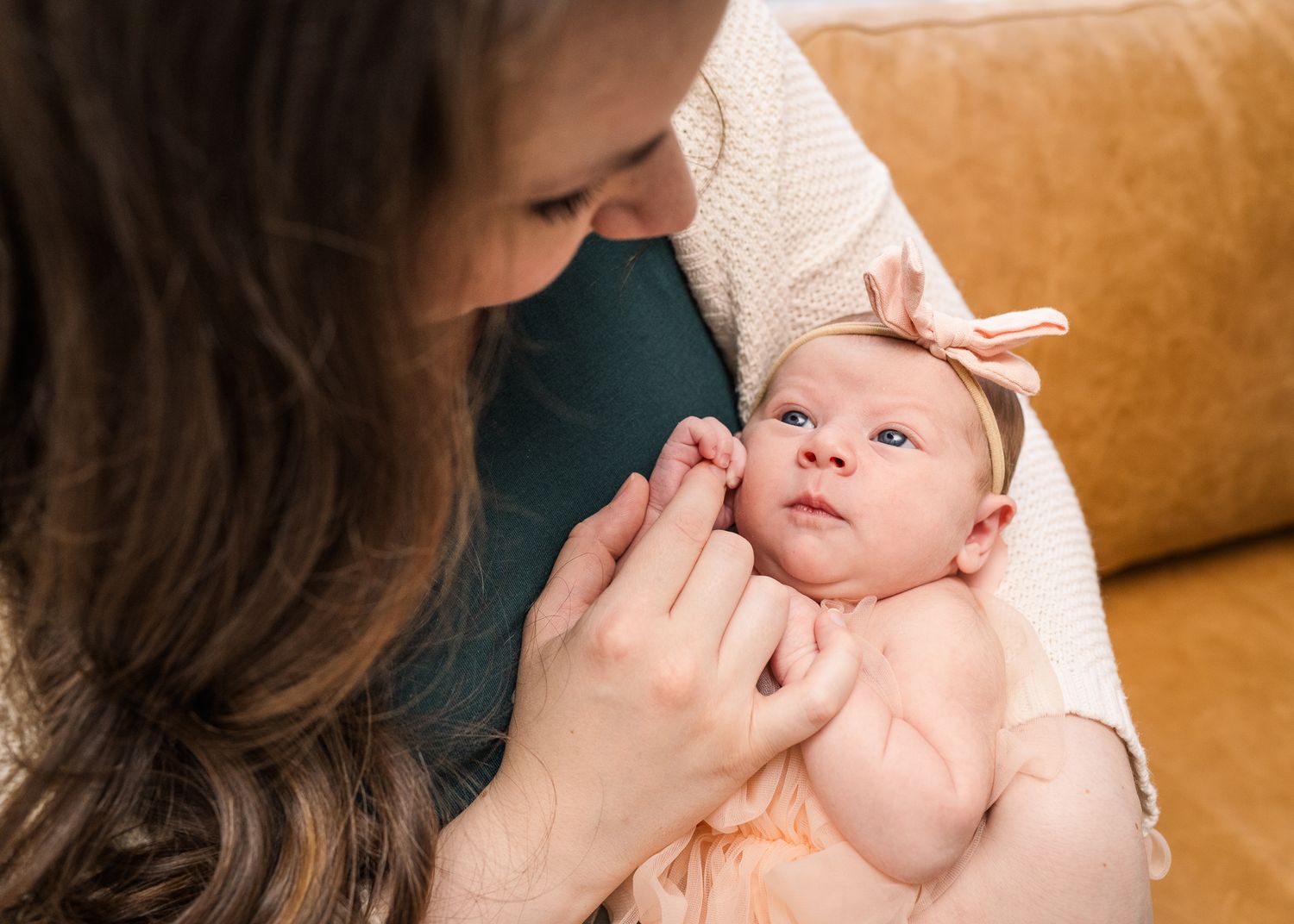 Close up of gentle interaction with alert newborn wearing bow.