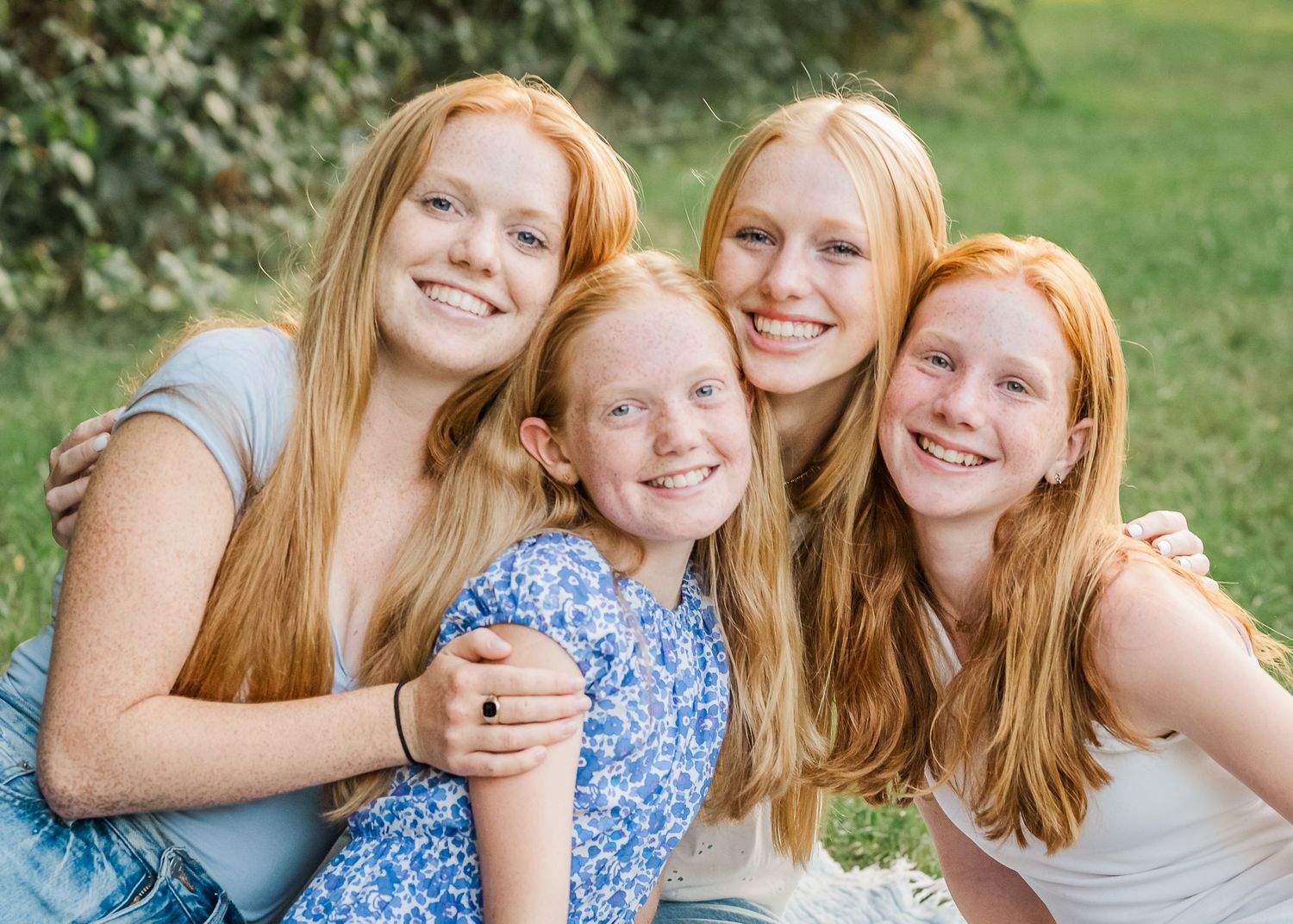Close-up portrait of four siblings with matching red hair smiling brightly outdoors.