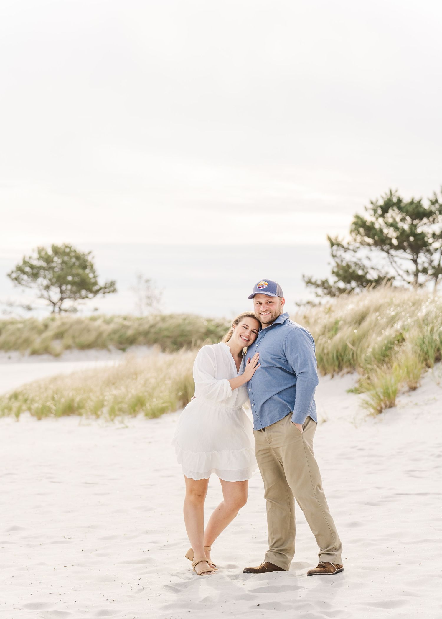 Romantic beach portrait of couple embracing on sandy dunes at sunset.