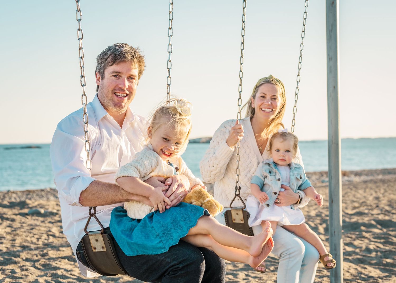 Family enjoying quality time together on a swing set by the beach during golden hour.
