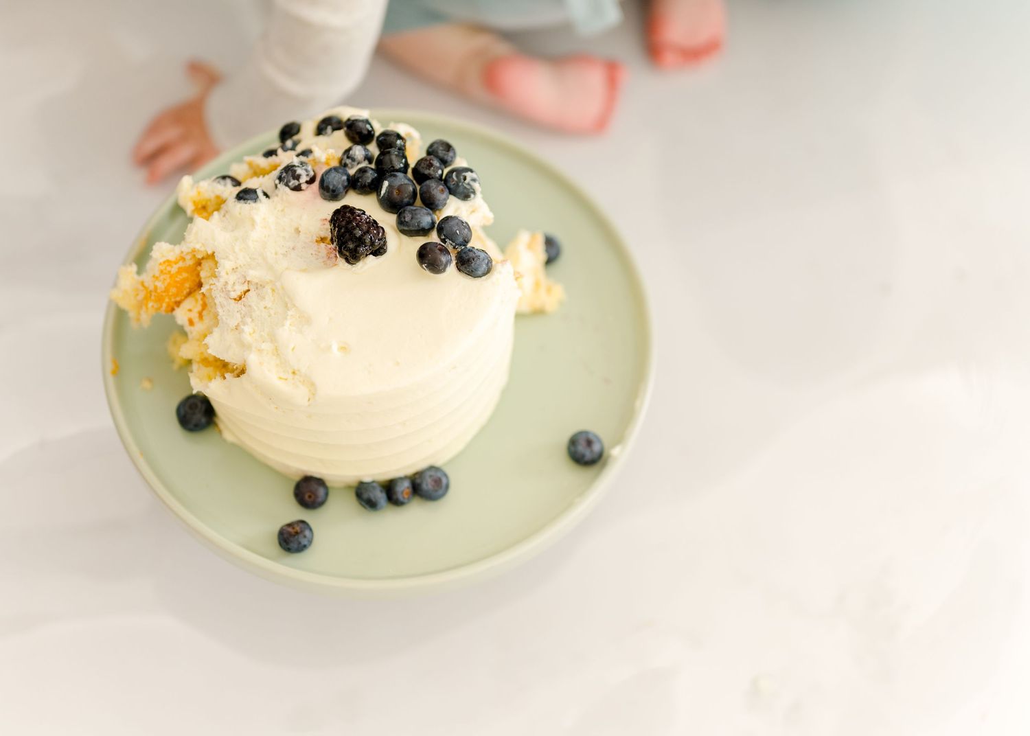 White cake with fresh blueberries and yellow garnish served on a pale green plate.