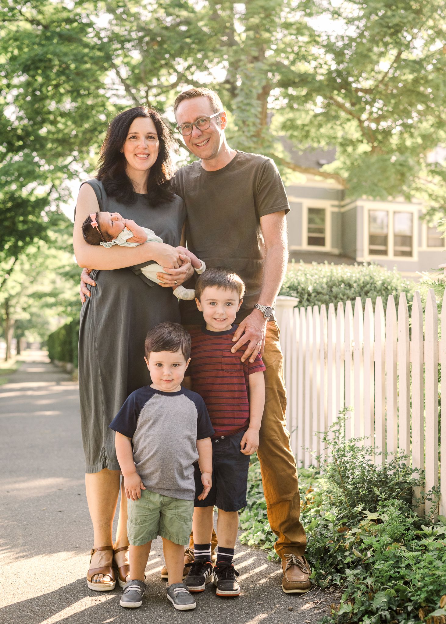 Family outdoor portrait in front of white picket fence and suburban home.