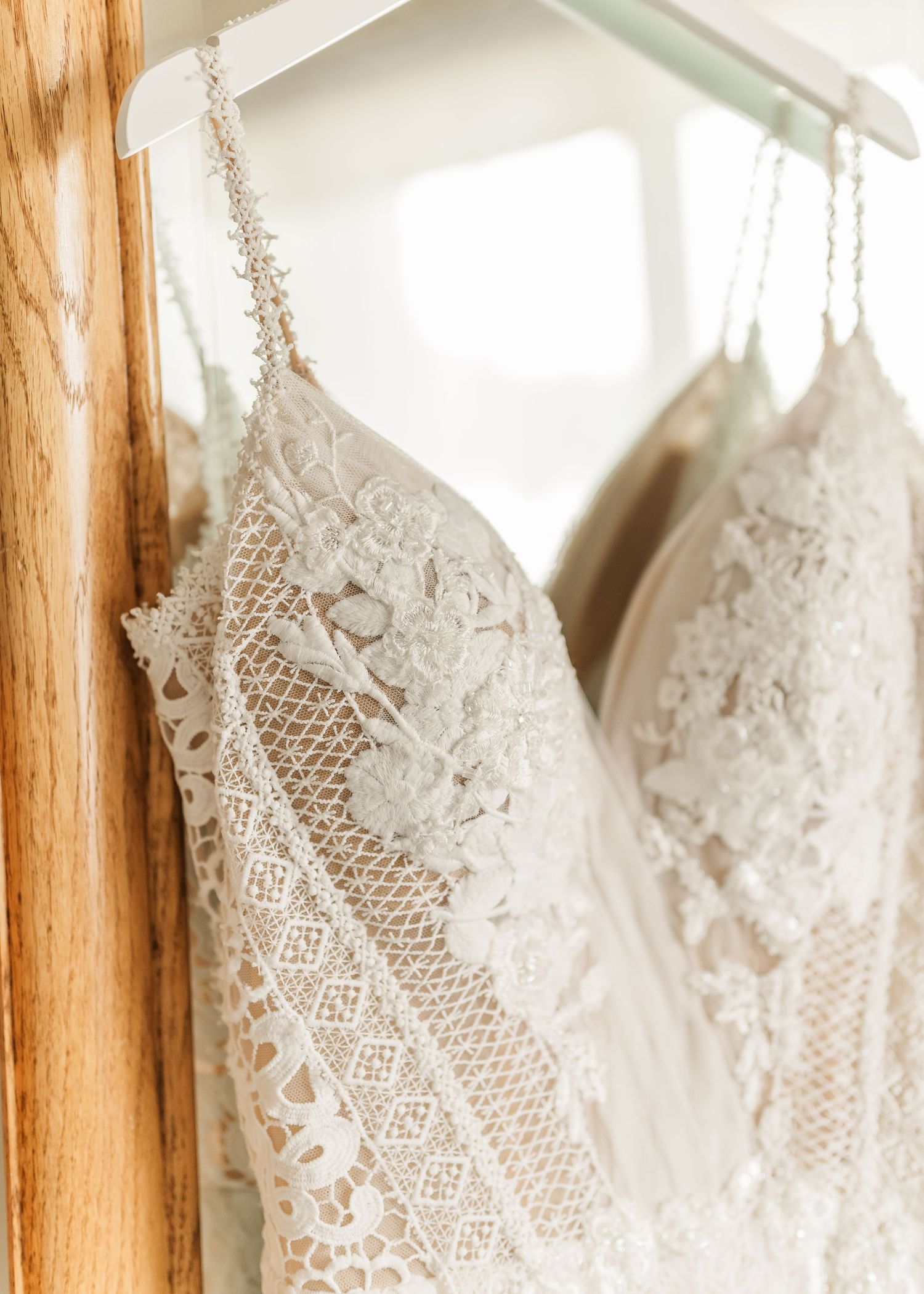 White lace wedding dresses hanging on wooden hangers in a bridal shop display.