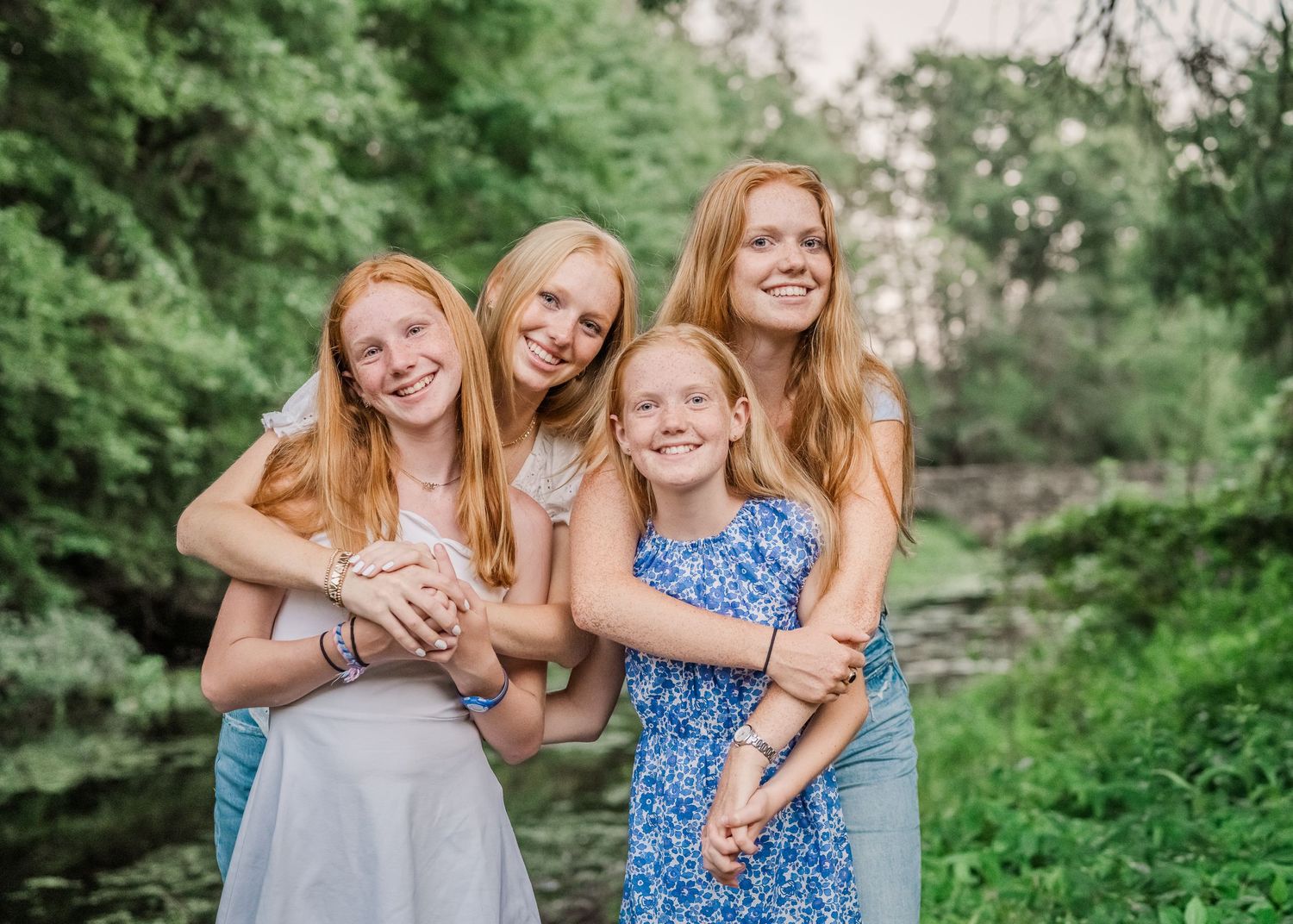 Four people with long red hair pose together in a green outdoor setting wearing casual summer dresses.