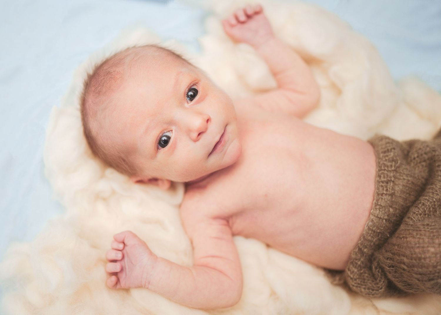 Infant lying on soft white fabric with bright eyes and peaceful expression.