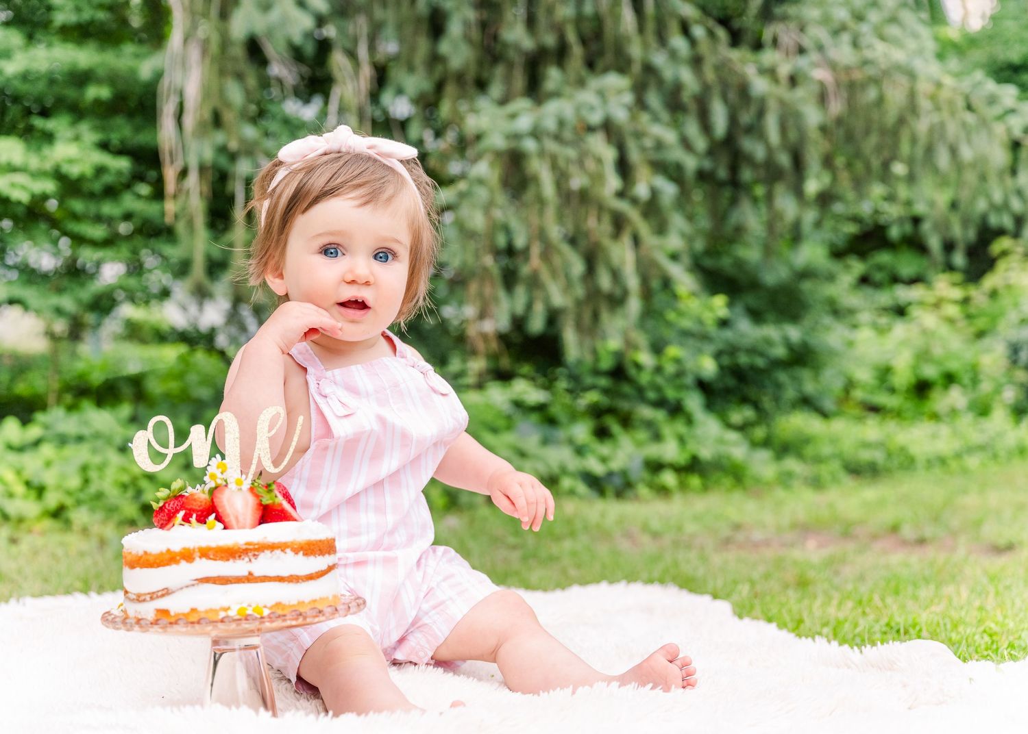 First birthday celebration with cake outdoors on a blanket.