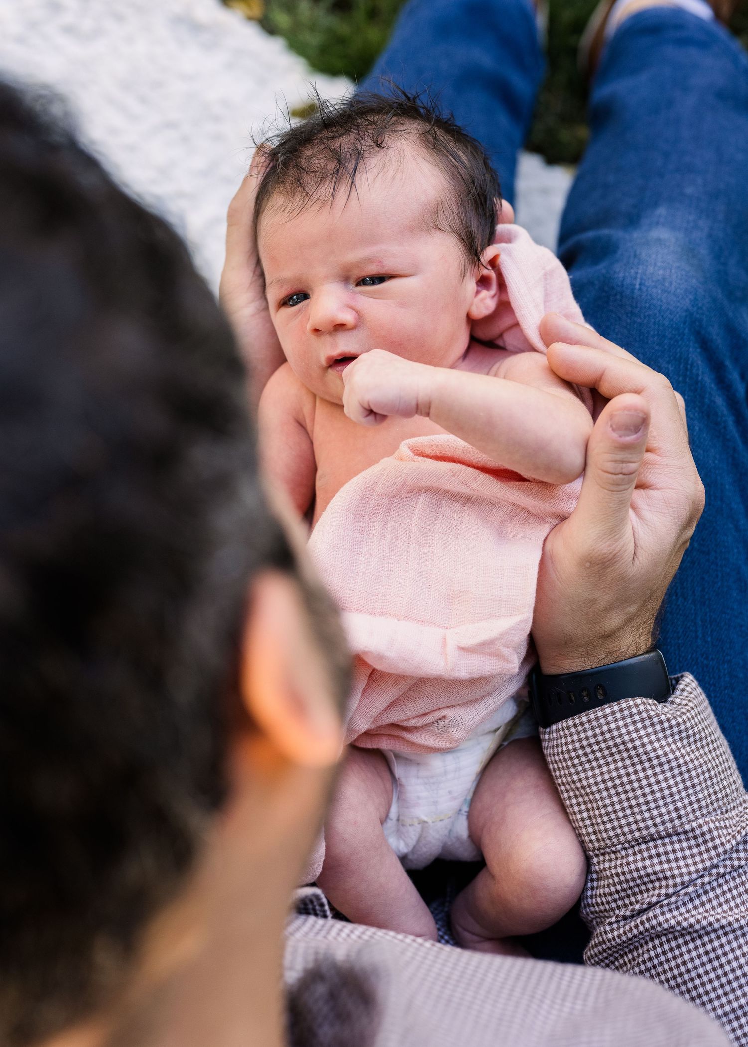 Newborn wearing pink outfit held gently by caregiver.