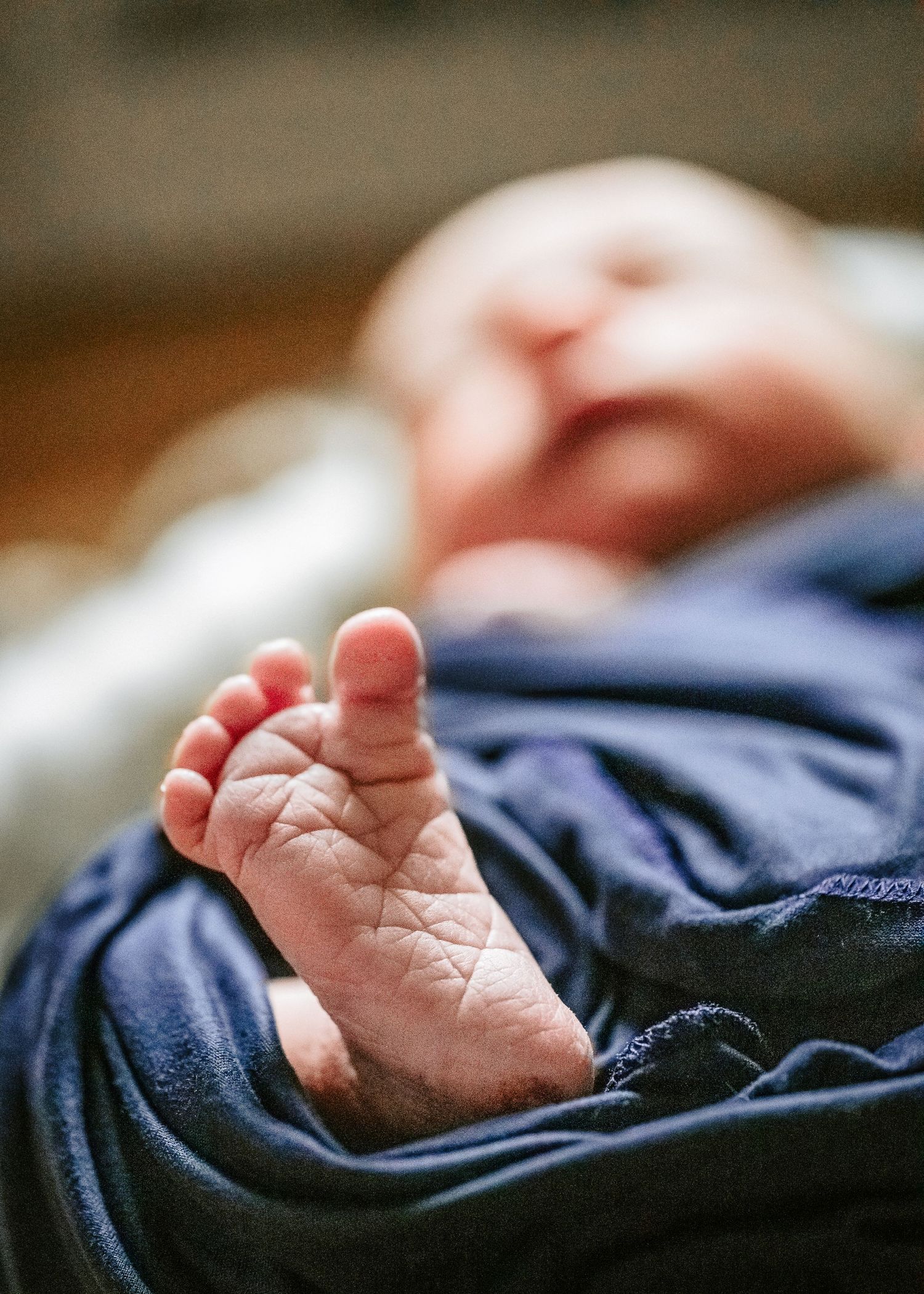 Tiny newborn baby foot with wrinkled sole against dark blue fabric background.