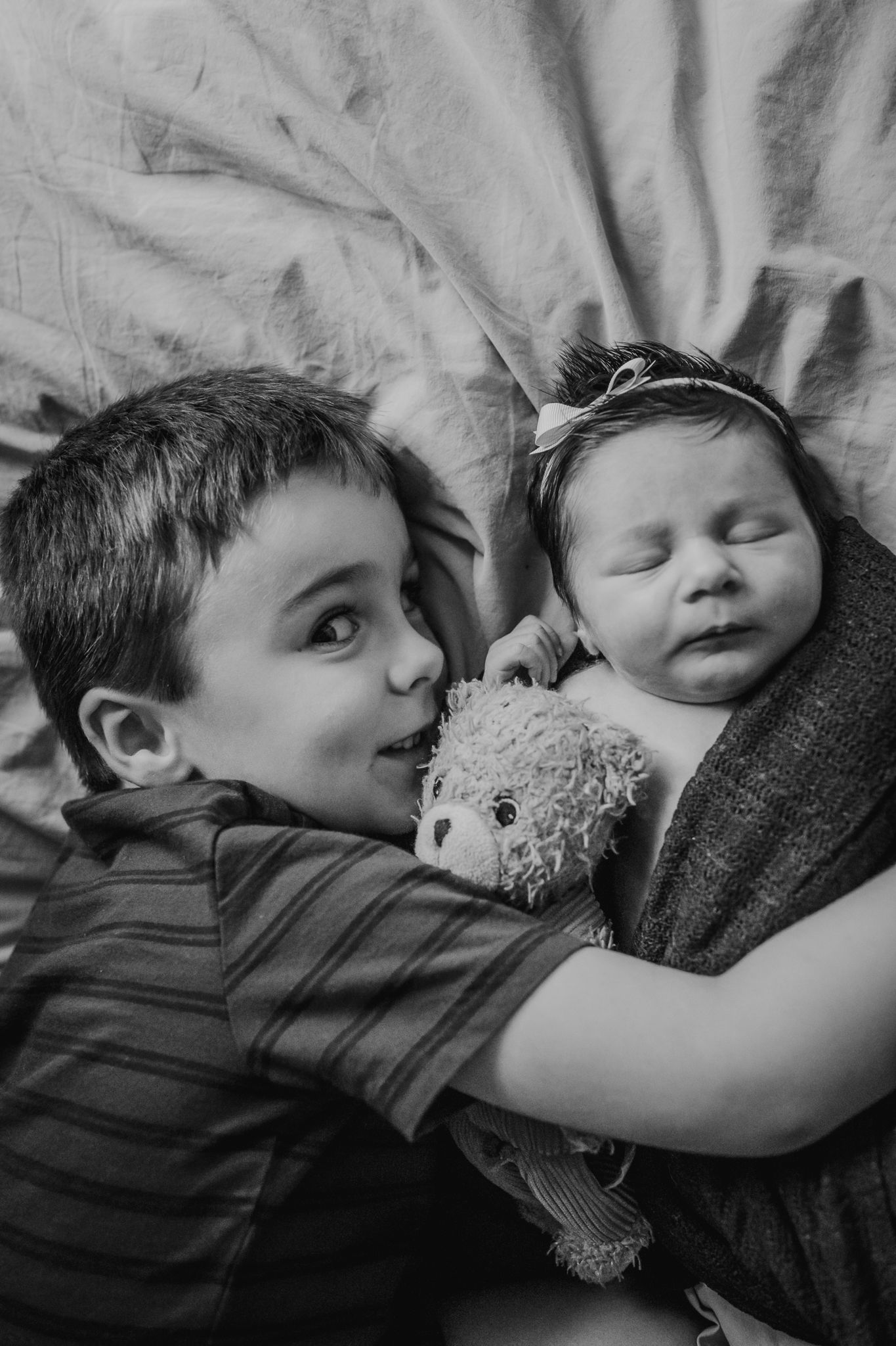 Black and white image of siblings bonding with stuffed toy bear.