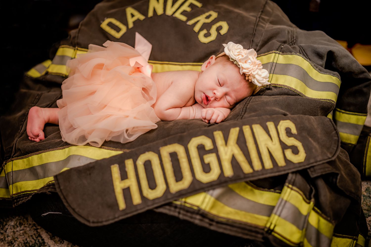 Newborn in tutu sleeping on firefighter uniform with Hodgkins name badge.