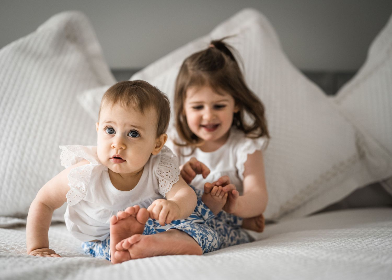 Two children in white outfits playing together on white bedding.