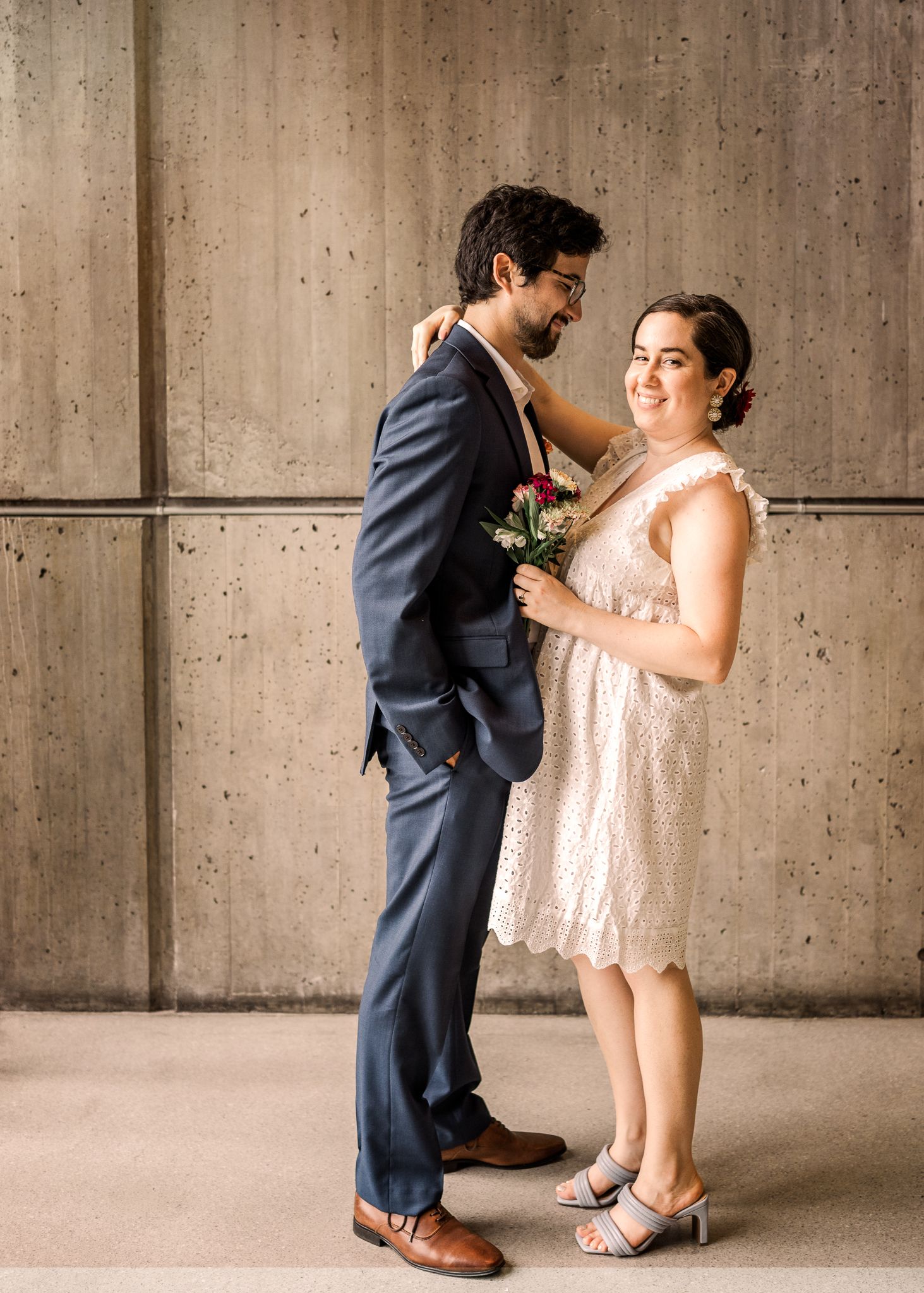 A couple poses together, the woman in a blush lace dress and man in a navy suit.