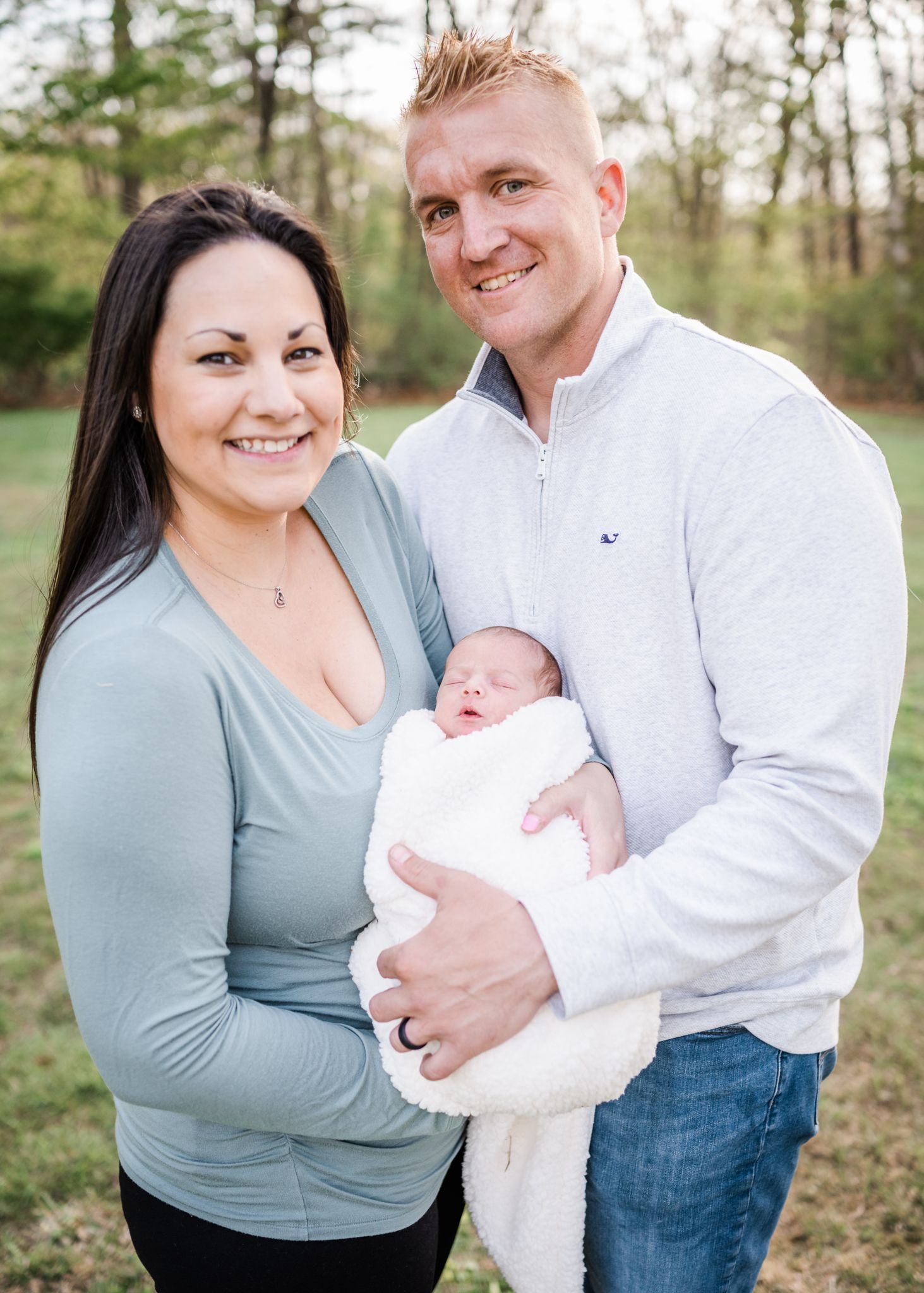 Happy family poses together outdoors while holding their newborn baby.