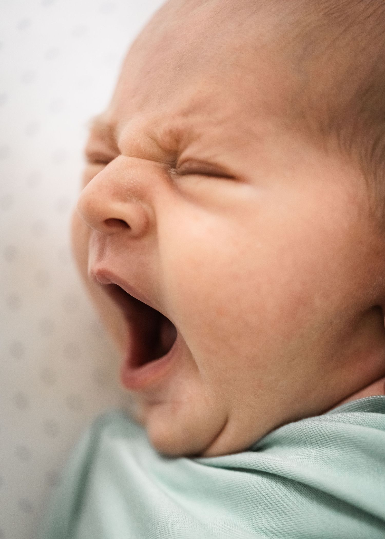 Close up of yawning baby's face against white background.