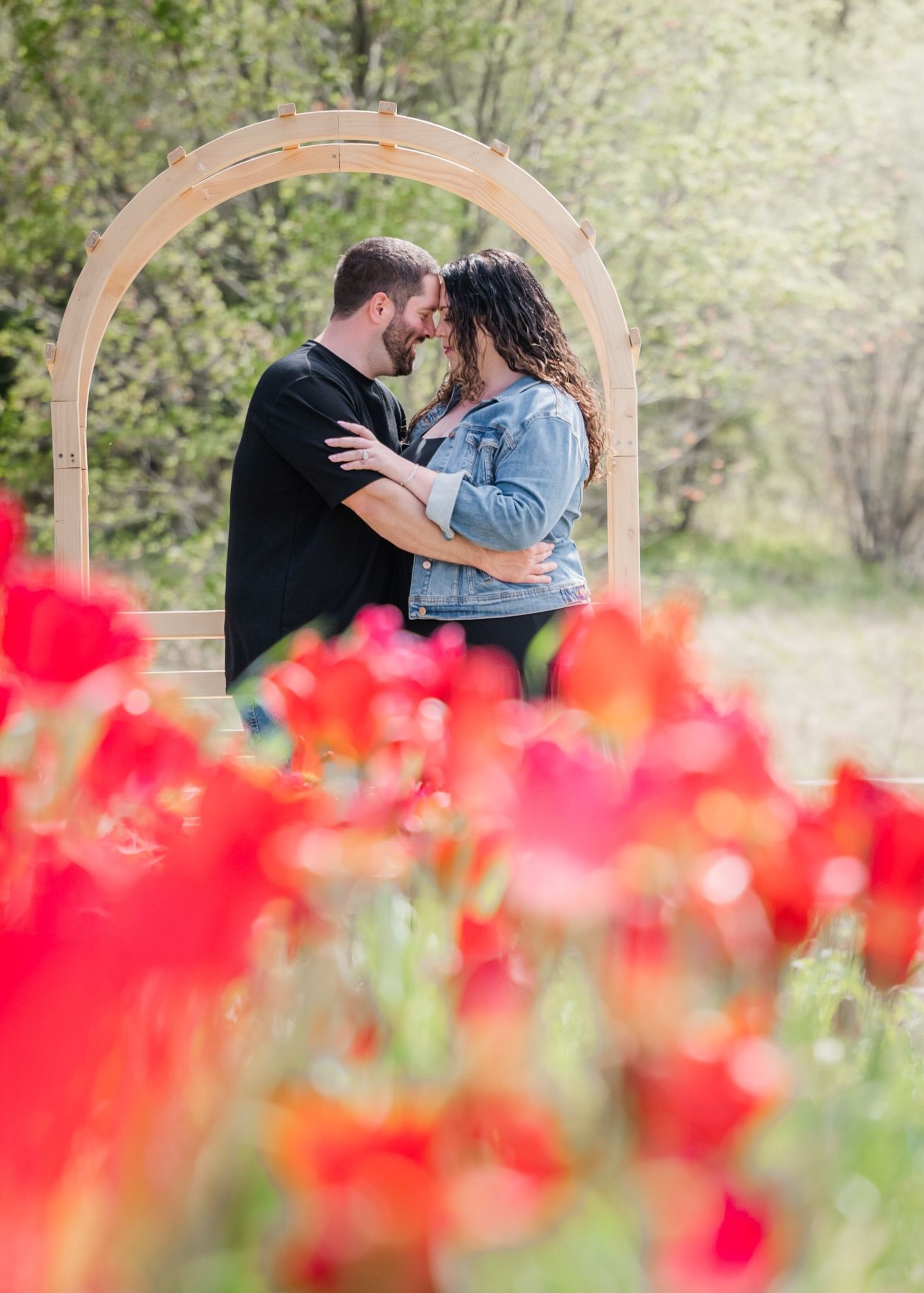Romantic couple embracing under a wooden arch surrounded by red tulips.