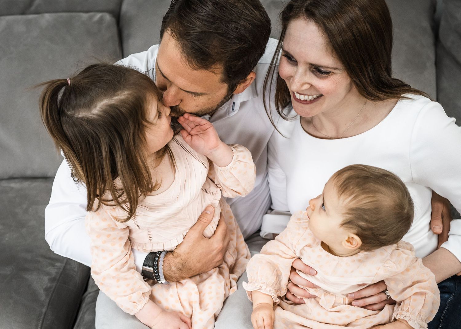 Tender family moment captured on gray couch with soft lighting.