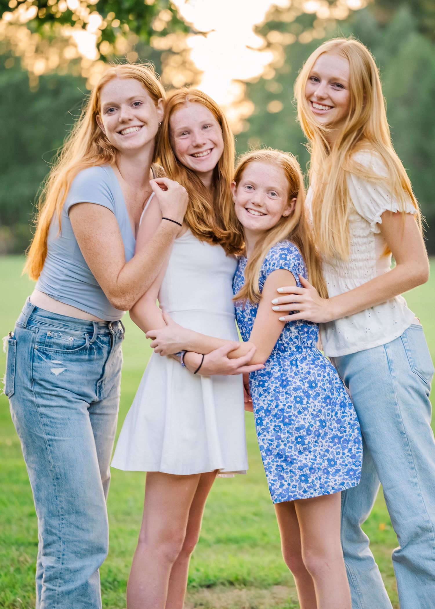 Four siblings embrace in a group hug while posing for an outdoor portrait at sunset.