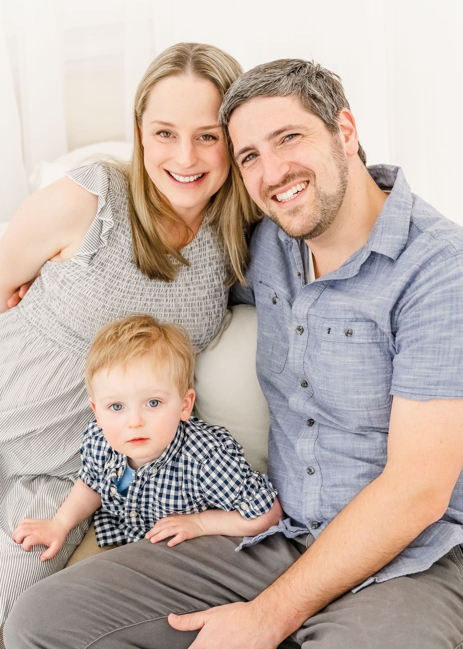 Portrait of a happy family of three sitting together, with a small toddler in a checkered shirt between two adults.