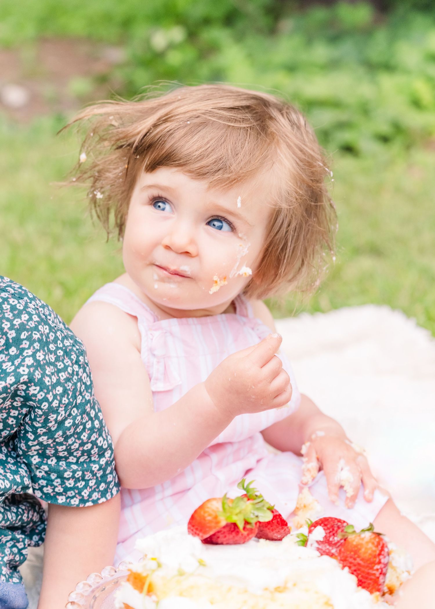 Pink party dress and fresh strawberries on white blanket in garden setting.
