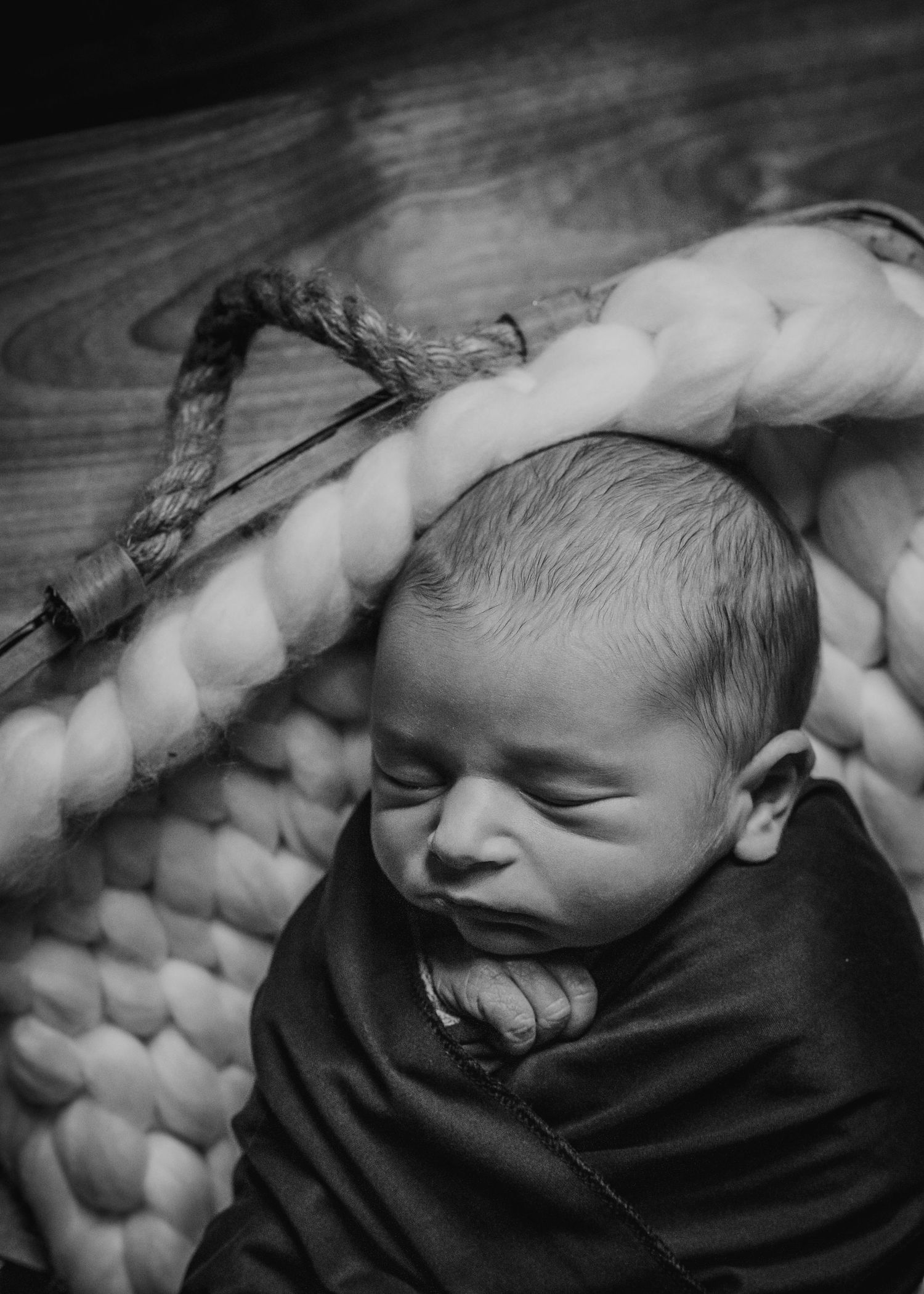 Black and white portrait of sleeping newborn on textured knit blanket.
