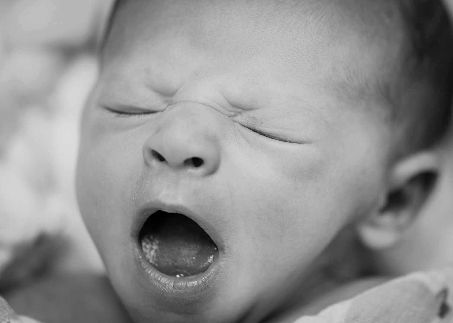 Close-up black and white photo of a yawning newborn with sleepy eyes closed.