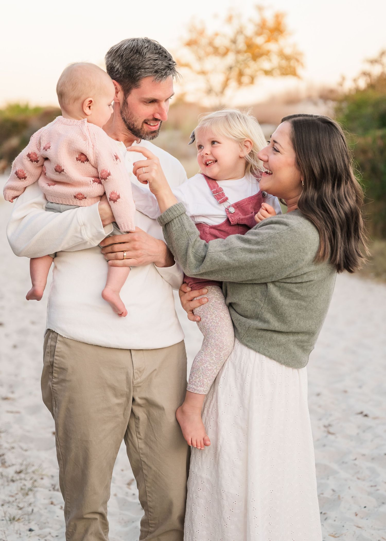Family shares joyful moments together on a beach during golden hour sunset photo session.