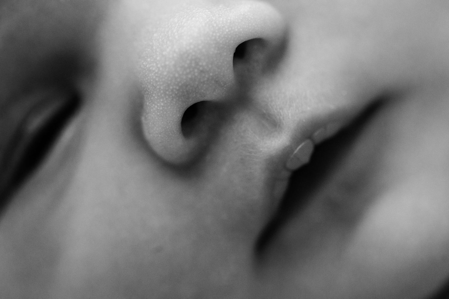 Close-up black and white macro photograph of a nose and mouth in soft focus.