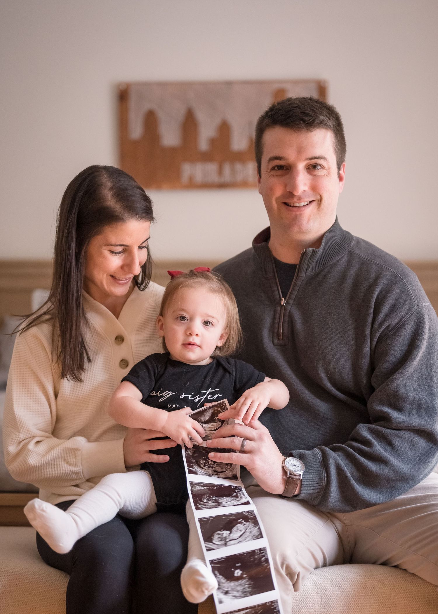 A family holds an ultrasound strip while sitting together on a couch.